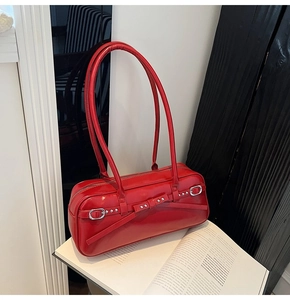 Close-up of a red leather underarm bag with glossy finish and metal buckle detail