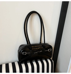 Close-up of black patent leather shoulder bag with silver buckles and metal rivets
