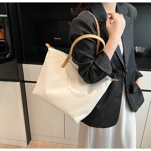 Detail of white nylon tote bag with brown leather handles worn by a model in a minimal setting
