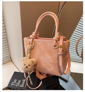 Pink glossy leather bucket bag detail with plush bear charm and adjustable strap