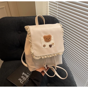 Detail of white glossy leather backpack featuring lace trim and brown plush bear patch