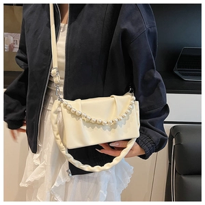 Détail d'un petit sac carré plissé crème avec chaîne perlée porté par un mannequin