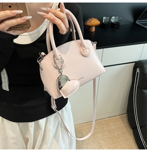 Detail of pink patent leather handbag with heart charm and delicate strap on a table