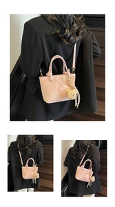 Detailed view of a pink matte leather bucket bag with top handles and a plush bear charm