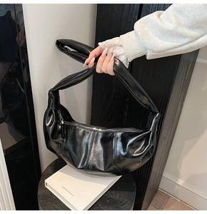 Close-up of shiny black crescent bag featuring pleated faux leather and a knotted strap