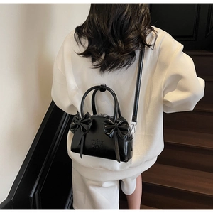 Vue détaillée d'un sac en cuir verni noir avec nœuds porté par un mannequin en escalier