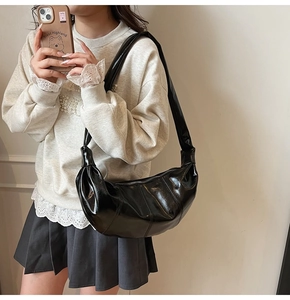 Detailed close-up of glossy black crescent shoulder bag with smooth faux leather texture
