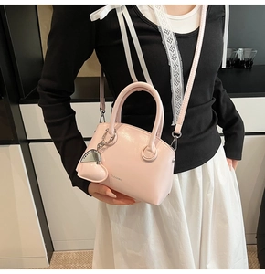 Detail of light pink crossbody bag with shiny leather texture and heart-shaped metal charm