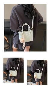 Detail view of mint green bucket bag featuring a plush bear charm and crossbody strap