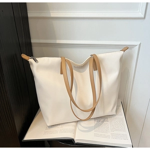 Detail of a cream nylon tote bag featuring brown leather handles and silver zipper closure