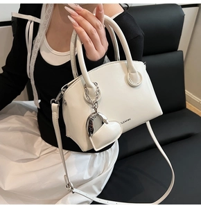 Detailed shot of white faux leather crossbody bag with heart charm and brand lettering