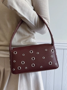 Deep burgundy underarm bag with silver grommets and lychee texture worn by a model
