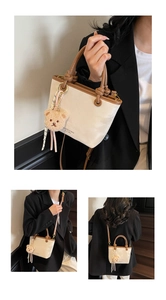Detail of cream bucket bag with brown handles, bear charm, and adjustable strap