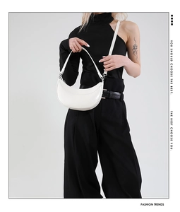 Sac demi-lune blanc avec détails argentés porté sur une tenue noire élégante