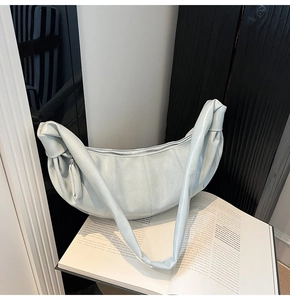 Close-up of light blue crescent bag featuring pleated texture and knot shoulder strap