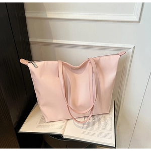 Detailed view of pink nylon tote bag with top zipper and metallic logo on a book