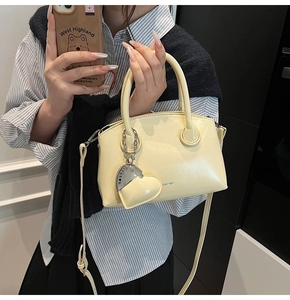 Detail view of cream Boston handbag with cylindrical handles and heart pendant