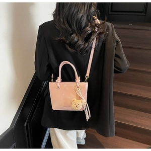 Detail of pink glossy bucket bag with teddy bear charm shown on a stylish outfit