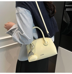 Close-up of a glossy cream tote bag featuring a heart charm and detachable strap