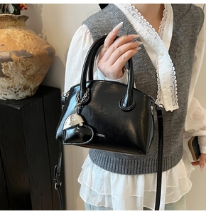 Detail of black patent leather bowling bag with silver logo and heart pendant
