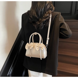 Détail du sac Boston blanc crème avec décoration de nœud et cuir texturé élégant