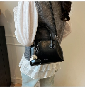 Detail of black glossy leather handbag with CLEA RVK logo and metallic heart charm