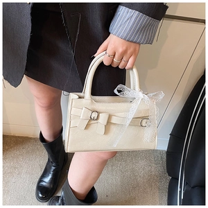 Dettaglio di una borsa bianco crema con chiusura a fiocco e nastro di pizzo sul manico