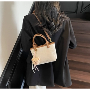 Detail view of cream and brown crossbody bucket bag with bear charm on a model