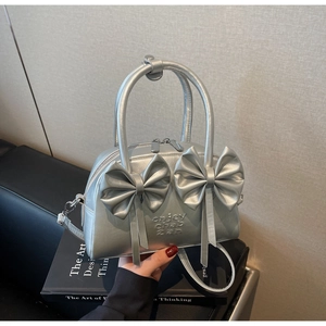 Détail du sac Boston argenté avec deux nœuds décoratifs sur un canapé en cuir noir