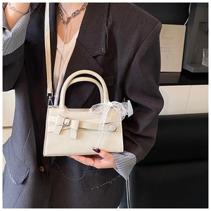 Dettaglio borsa a mano color crema con fibbia a fiocco e decorazioni in pizzo bianco