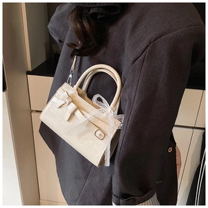 Dettaglio borsa beige con fibbia a fiocco e pizzo indossata su un blazer grigio