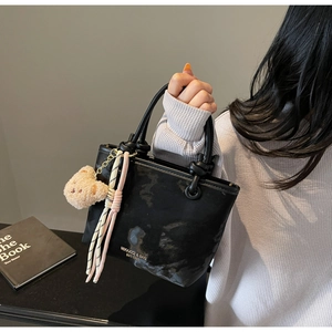 Detail of black bucket bag featuring metal ring hardware and a plush bear pendant charm