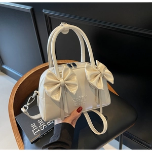 Détail d'un sac à main blanc crème avec nœuds, ferrures argentées et cuir synthétique