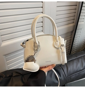 White minimalist leather handbag with circular handles and a heart charm accessory