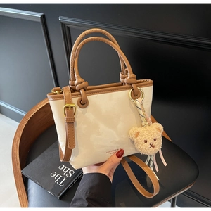 Detail view of cream bucket bag with brown trim, logo print, and plush bear charm