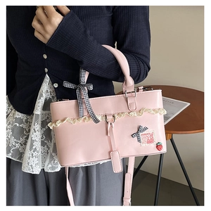 Detail of pink PU leather bag with white lace, checkered bow, and strawberry charm