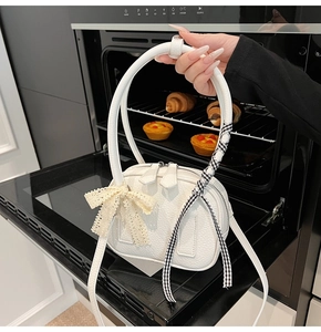 Close-up of white lychee leather handbag with lace bow and plaid ribbon handle detail