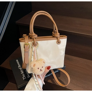 Detail of cream bucket bag with brown leather handles and plush bear charm on wood