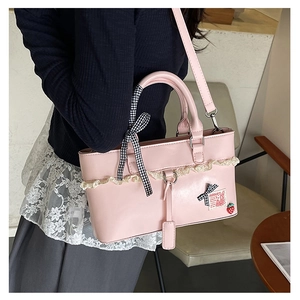 Detail of pink PU leather handbag featuring lace trim, bow ribbon and strawberry pendant