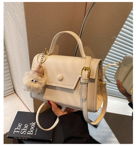 Dettaglio della borsa beige minimalista con fibbia rotonda e ciondolo di peluche