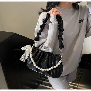 Detail view of black pleated underarm bag with white pearl chain and lace bow accent