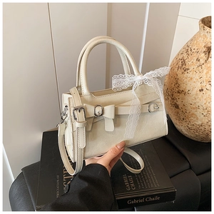Dettaglio di una borsa bianco crema con eleganti fiocchi in pelle e pizzo tenuta in mano