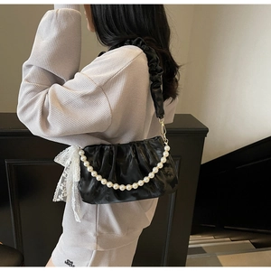 Detail of black pleated shoulder bag with pearl chain and white lace bow decoration