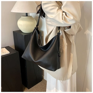 Model wearing a large black pebbled leather tote bag with a minimalist half-moon shape