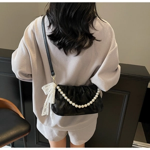 Detail of a black ruched shoulder bag featuring pearl chains and a white lace bow charm