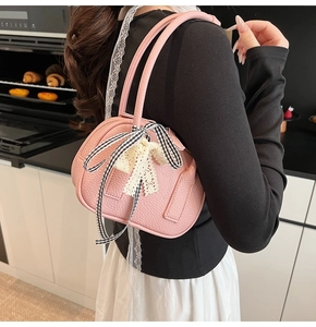 Pink bowling handbag with black and white bow and lace details worn by model in a kitchen