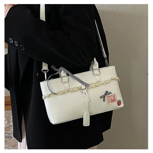 Detail of white PU leather handbag with lace trim and strawberry charm on black suit