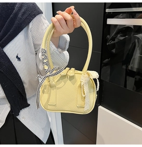 Close-up of yellow pebble leather handbag with lace bow detail and circular handle
