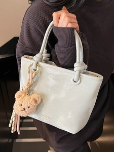 Minimalist grey bucket bag with contrast knot handles and brown teddy bear charm