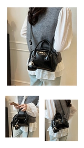 Detail view of glossy black Boston bag with round handles and a heart-shaped charm